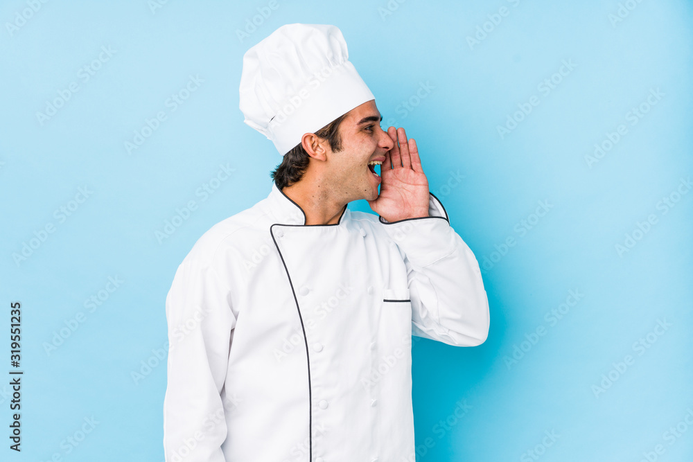 Young cook man isolated shouting and holding palm near opened mouth.