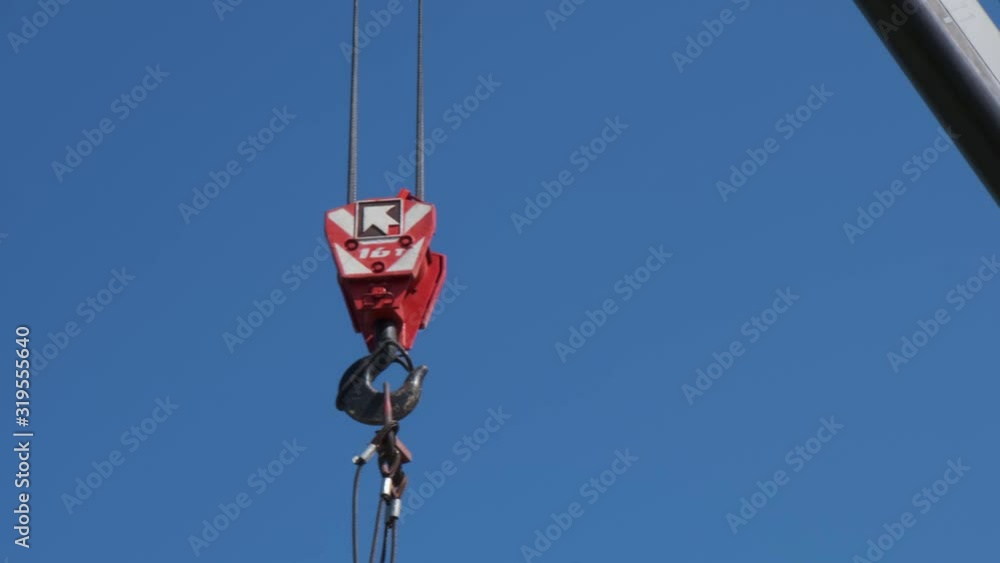 The red hook of a construction crane hanging down from a boom on a clear sky The red hook of a construction crane hanging down from a boom on a clear sky