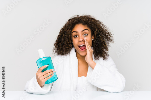Young african american woman holding a mouth wash shouting excited to front.