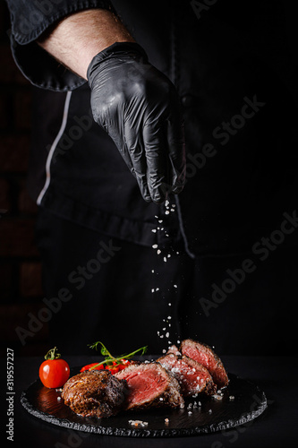 The concept of cooking meat. The chef cook salt on the cooked steak on a black background, a place under the logo for the restaurant menu. food background image, copy space text