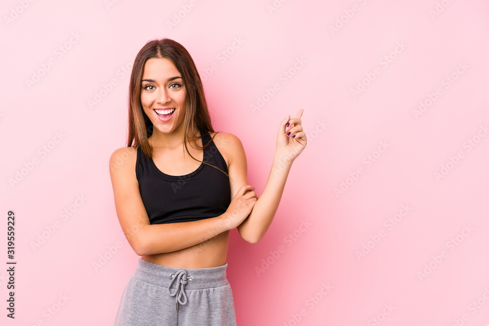 Young caucasian fitness woman posing in a pink background smiling cheerfully pointing with forefinger away. Young caucasian fitness woman posing in a pink background smiling cheerfully pointing with forefinger away.
