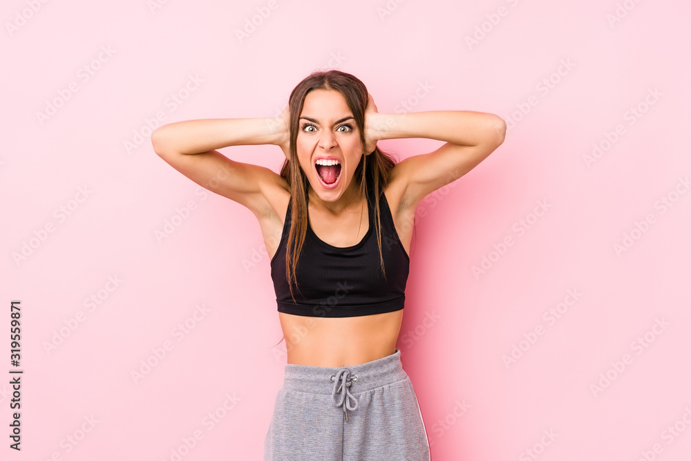 Young caucasian fitness woman posing in a pink background covering ears with hands trying not to hear too loud sound. Young caucasian fitness woman posing in a pink background covering ears with hands trying not to hear too loud sound.