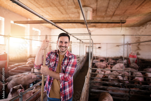 Pig farming. Shot of smiling farmer worker standing in pig pen at the cattle farm.