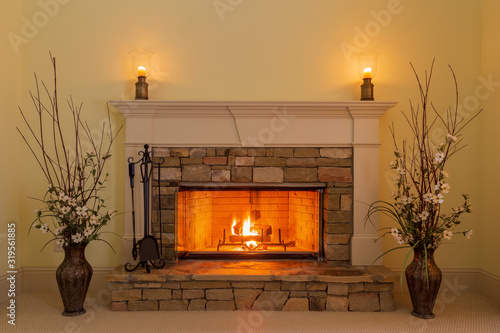 Cozy fire in a stone fireplace in a residential home with candles and flowers.