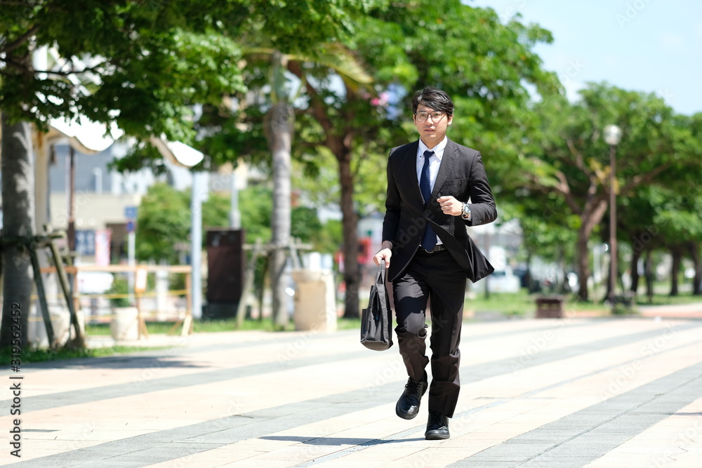 朝の駅前でスーツ姿の眼鏡をかけた20代の日本人の男性が走る