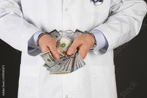 Doctor in handcuffs with bribe on black background, closeup. Corrupted medicine