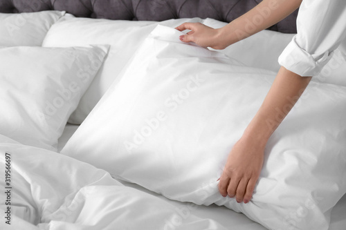 Woman fluffing soft pillow in bedroom, closeup