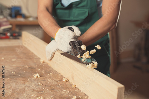 Professional carpenter grinding wooden plank with jack plane in workshop, closeup