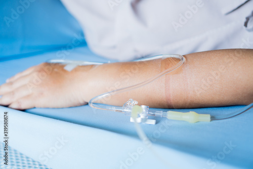 Patients saline, Iv drip, young woman hand with medical drip intravenous needle, give salt water on hospital bed. intravenous therapy (IV) is a therapy that delivers fluids directly into vein.