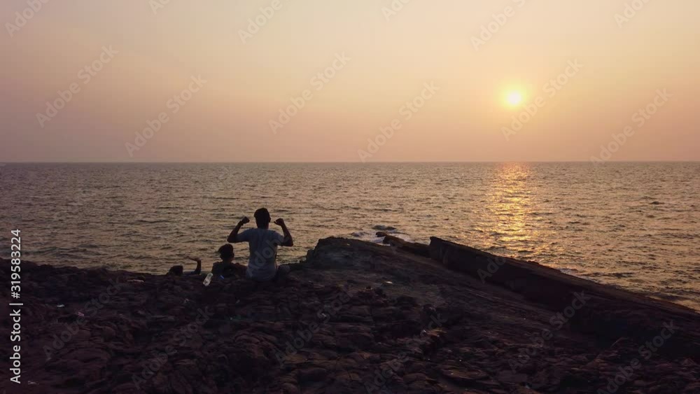 Friends sit on a cluttered rock near the sea and watch the sunset Friends sit on a cluttered rock near the sea and watch the sunset