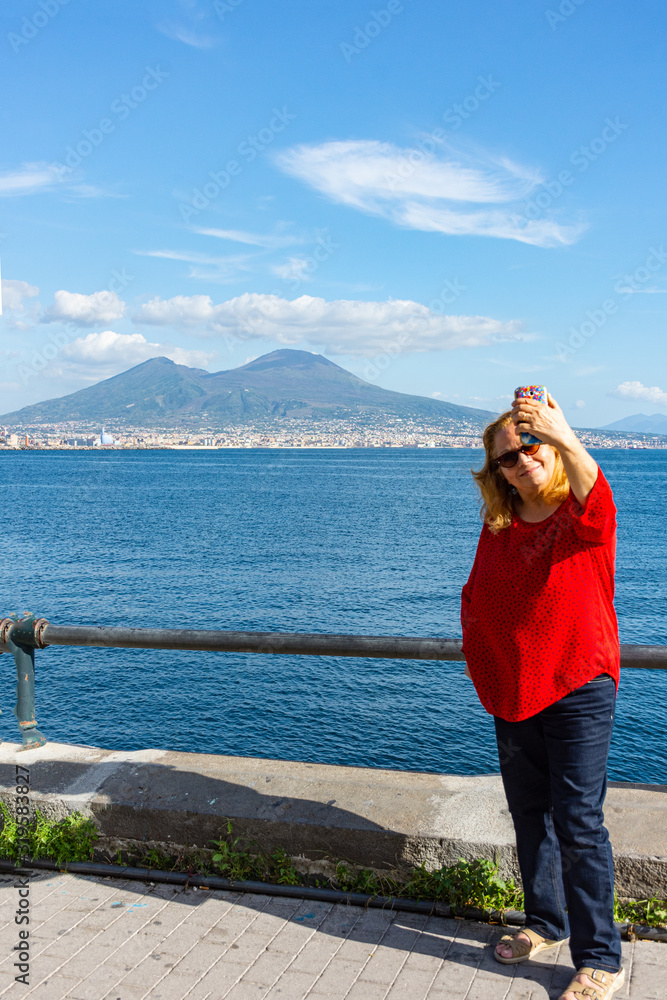 Italy, Naples, 7 October 2019, blonde tourist posing on the waterfront with Vesuvius in the background.