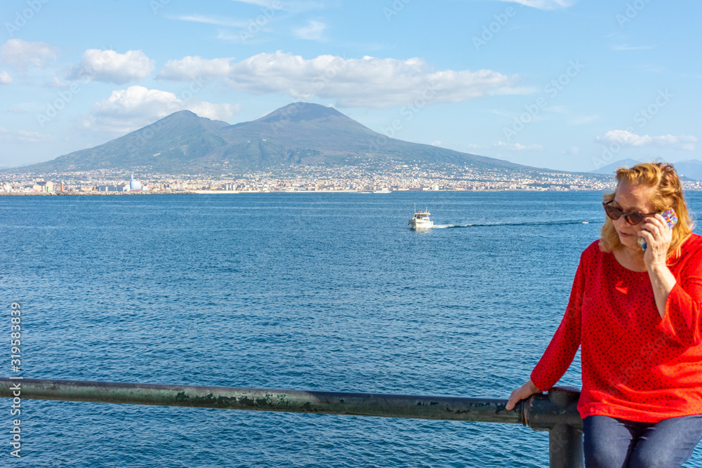 Italy, Naples, 7 October 2019, blonde tourist posing on the waterfront with Vesuvius in the background.