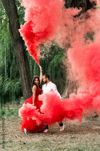 Beautiful romantic couple. Young woman in red dress and crown with handsome man in white shirt are dancing with pink smoke.Baby gender Happy Saint Valentine's Day.Pregnant and wedding concept.