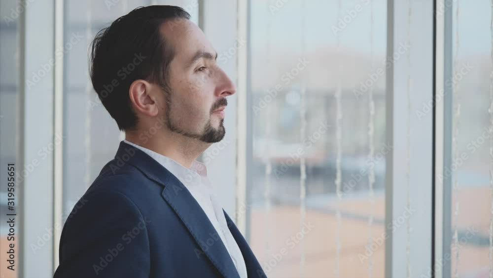 Businessman in formal suite stands in front of panoramic window with city view. Profile view. Outboard profile. Close up. Animation. 4K. Businessman in formal suite stands in front of panoramic window with city view. Profile view. Outboard profile. Close up. Animation. 4K.