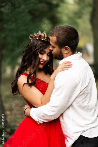 Beautiful romantic couple kiss closeup. Attractive young woman in red dress and crown with handsome man in white shirt are in love. Happy Saint Valentine's Day. Pregnant and wedding concept.