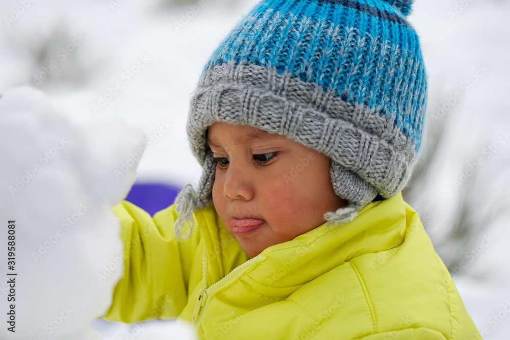 A kid that is concentrated as he makes a snowman and is wearing winter clothes in the snow. A kid that is concentrated as he makes a snowman and is wearing winter clothes in the snow.