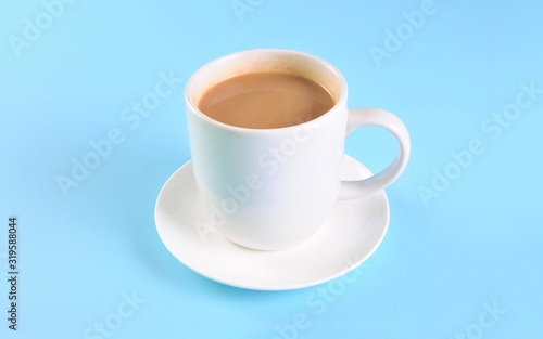 White cup of creamy coffee isolated on blue background.