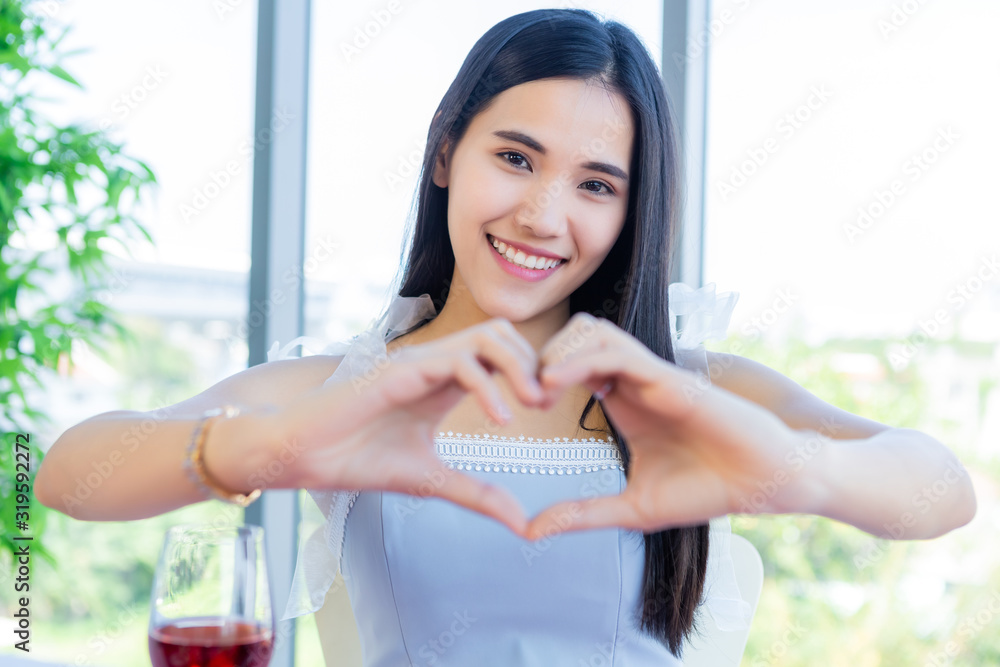 Valentine's day concept, a heart shape handmade of happy Asian young female sitting at a table food with wine glasses and bouquet of red and pink roses at in the restaurant background Valentine's day concept, a heart shape handmade of happy Asian young female sitting at a table food with wine glasses and bouquet of red and pink roses at in the restaurant background