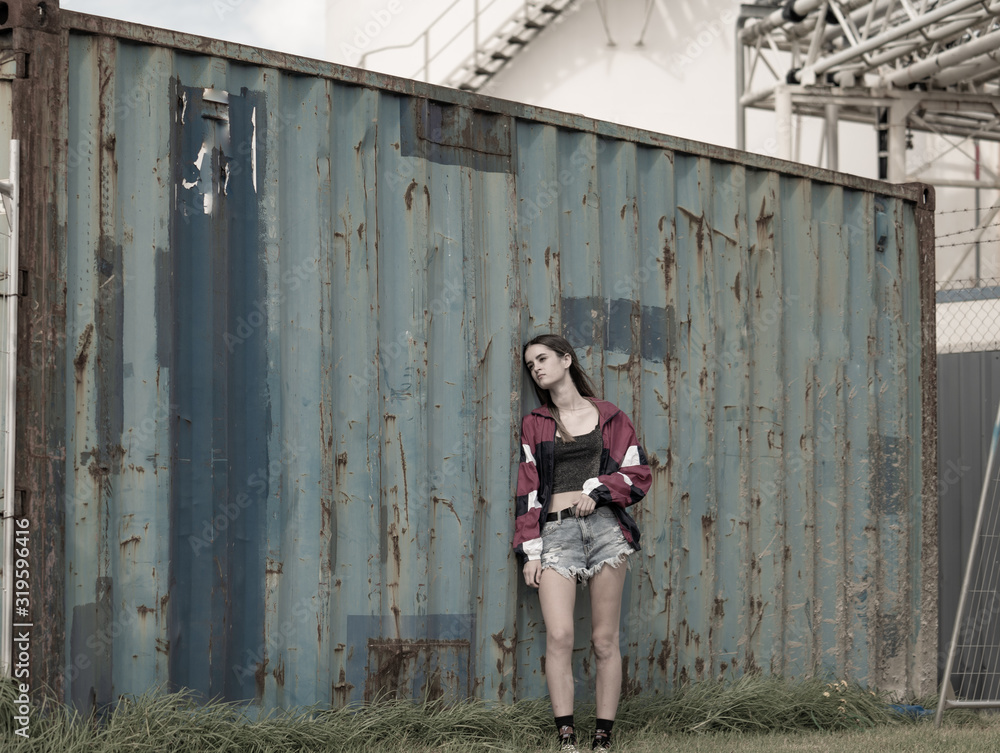 Modern teenager girl standing by old cargo container