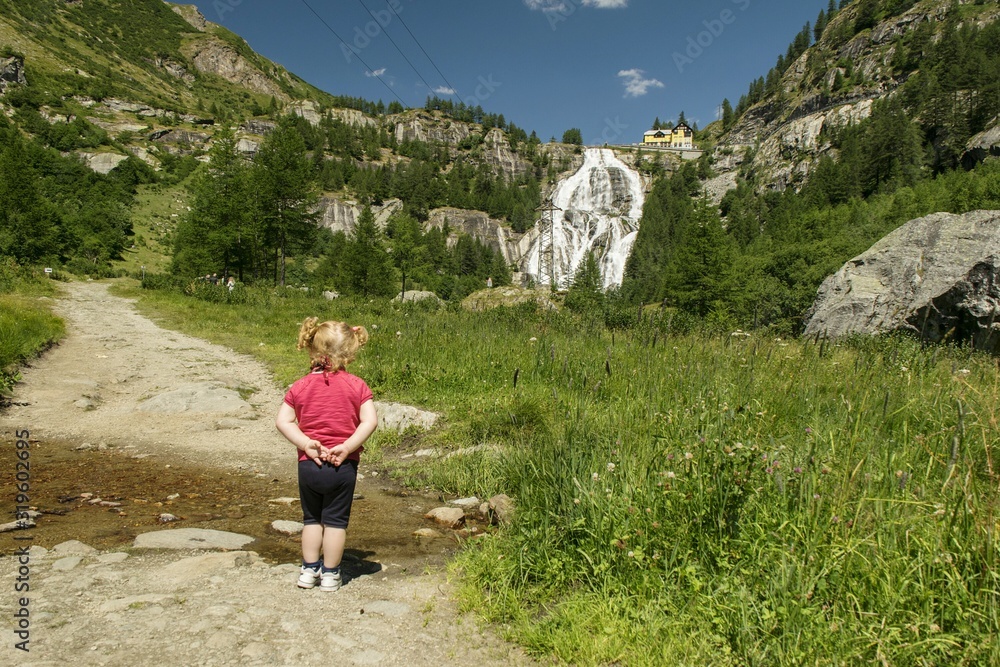 Rear View Of Baby Girl Standing Against Waterfall - obrazy, fototapety, plakaty 
