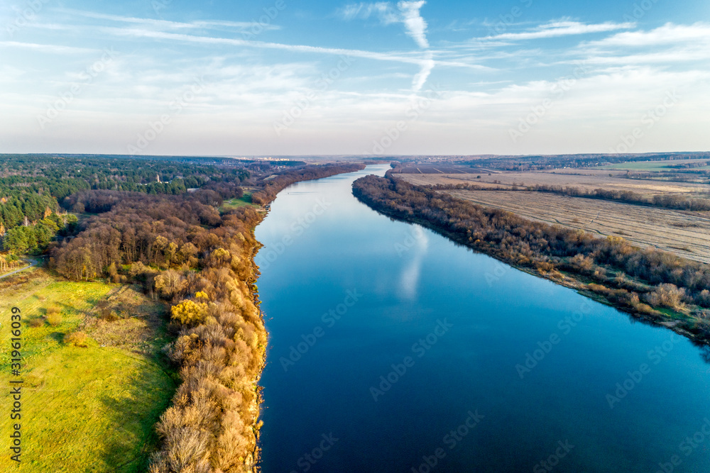 The bend of a wide river flowing among fields and forests. Autumn landscape, aerial view.