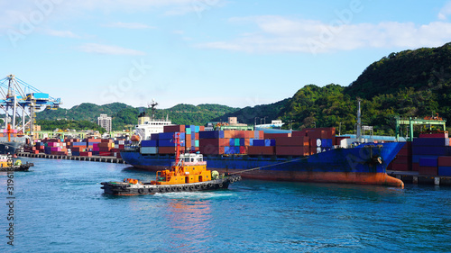Work in container terminal of port. two powerful towboats help container ships sail from the port after loading with multi-colored containers in turquoise ocean water. Taiwan