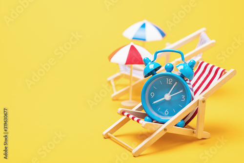 Alarm clock in a deck chair with a parasol on a yellow background with copy space. Concept on the theme, time to relax