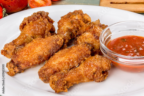 Fried breaded chicken wings served with sauce on a white plate