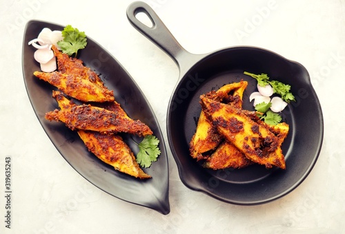 Marinated Pomfret fried fish or Indian Spicy fish fry garnished with onion and coriander on iron skillet griddle, selective focus with copy space.