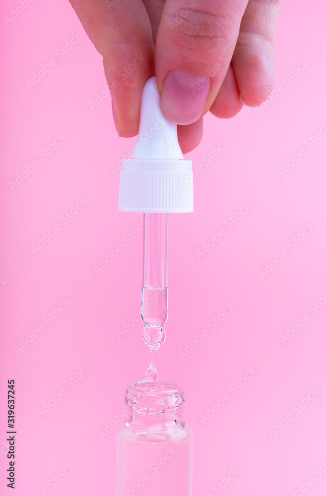 Female hand holds a dropper with serum on pink background. Female hand holds a dropper with serum on pink background.