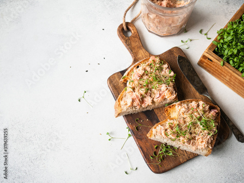 Healthy toasts with salmon pate and fresh green sprouts on yeast-free bread on wood cutting board on grey background. Copy space photo