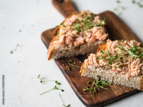 Healthy toasts with salmon pate and fresh green sprouts on yeast-free bread on wood cutting board on grey background.