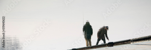 Blurry silhouette reflection in water of two people standing on a river dock