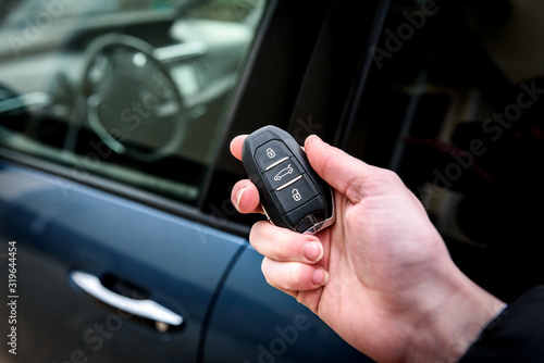 Hand holding a car key with remote control and pushing a button, he is unlocking the door.
