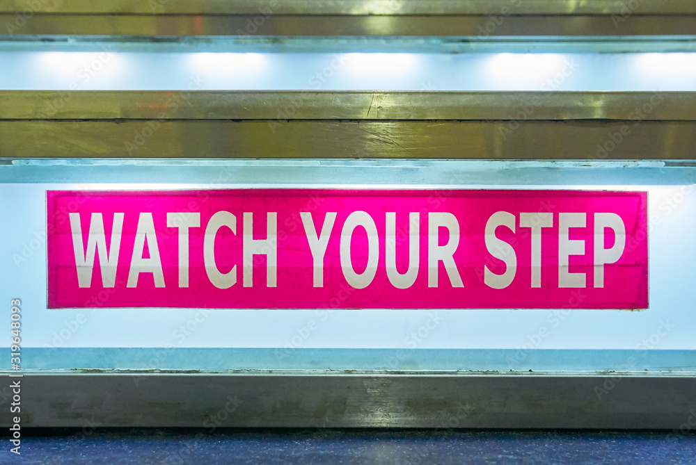 Close-up of a pink colored Watch Your Step sign taped to a staircase, which is illuminated with neon light, seen on a ferry ship in the Philippines Close-up of a pink colored Watch Your Step sign taped to a staircase, which is illuminated with neon light, seen on a ferry ship in the Philippines