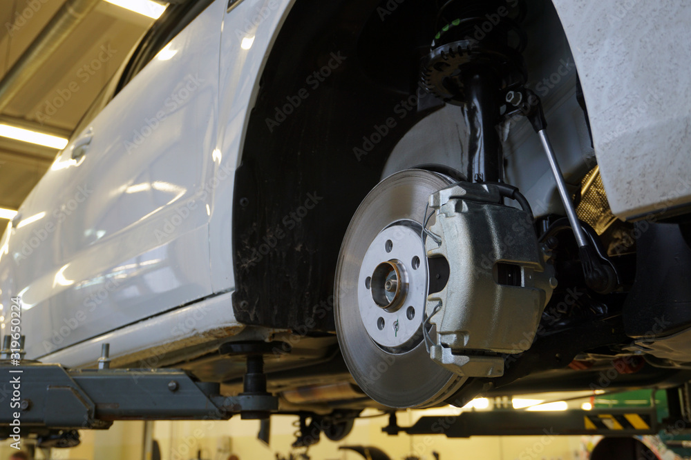A modern luxury car at a service station is lifted on a lift for repair. Front brake disc, caliper. Quality after-sales service concept. A modern luxury car at a service station is lifted on a lift for repair. Front brake disc, caliper. Quality after-sales service concept.