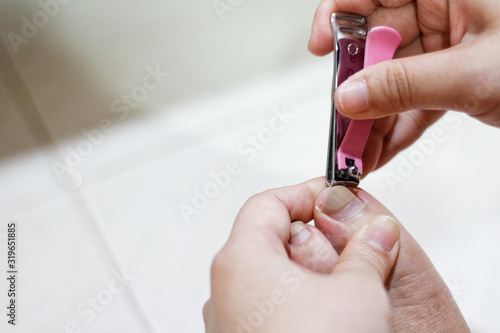 Asian woman cutting pedicure With a pink nail cutter. Painted toenails.
