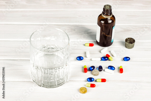 Close-up of bright colored medical tablets, a bottle of medicine and capsules with medicines and a glass of water. Scattered on the table Pills from the first-aid kit box. Toned. Copy space