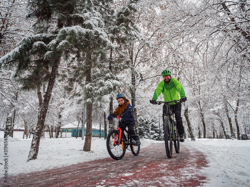 Man and his son ride bicycles along a bicycle path in a winter park. Father and son spend an active weekend in the park