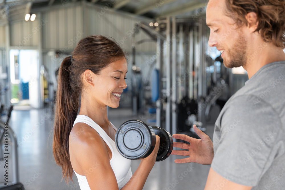 Fototapeta premium Gym workout personal trainer man helping woman having the right body posture to lift dumbbell weights. Exercise fit lifestyle.