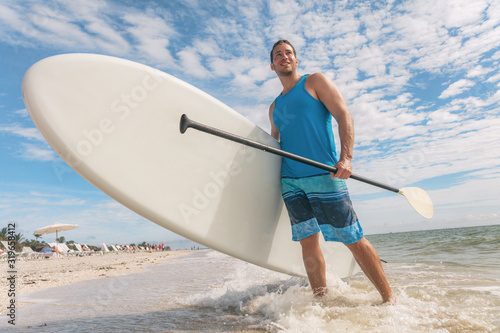 Photography Paddle board fun SUP watersport fitness man carrying paddleboard after water surf session in Sanibel Island, Florida
