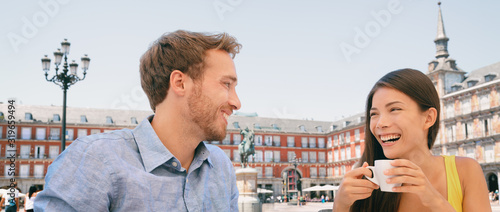 Couple drinking coffee at Madrid cafe dating laughing panoramic banner. Two tourists peaple having fun conversation talking on outdoor Plaza Mayor terrace summer travel vacation. Young woman and man. photo