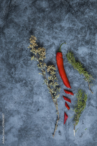 An assortment of red chilli pepper with thyme and rosemary over a dark surface in vertical