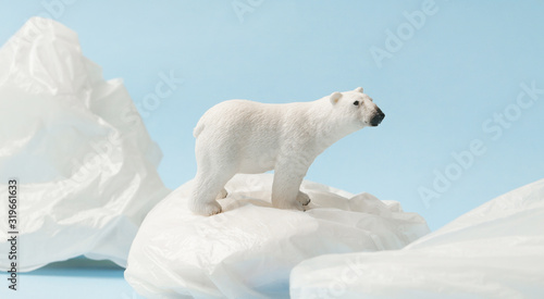 White polar bear on plastic bag on blue background, plastic pollution and climate change concept