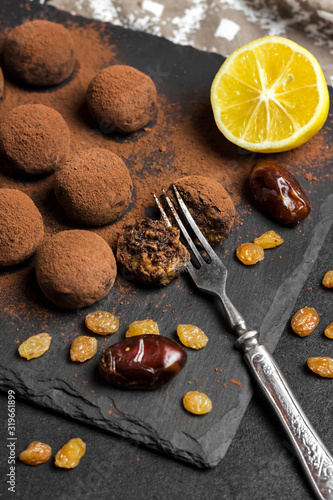 Homemade vegan truffles with dried fruits, walnuts and raw cocoa powder served on black slate plate.