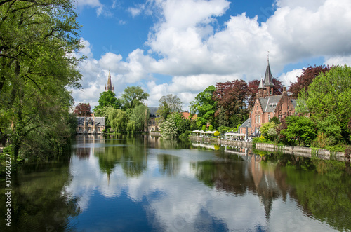 View of tranquil public green space featuring Minnewater Lake and small castle in Bruges during sunny day in spring, Belgium