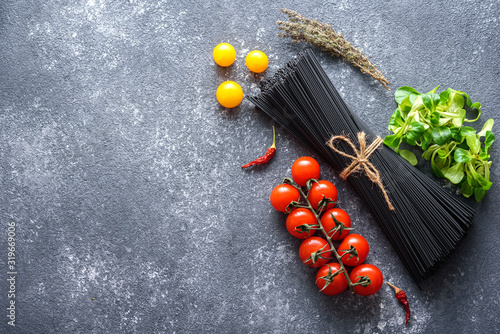ingredients for Italian dinner - black spaghetti with cuttlefish ink, vegetables on gray background