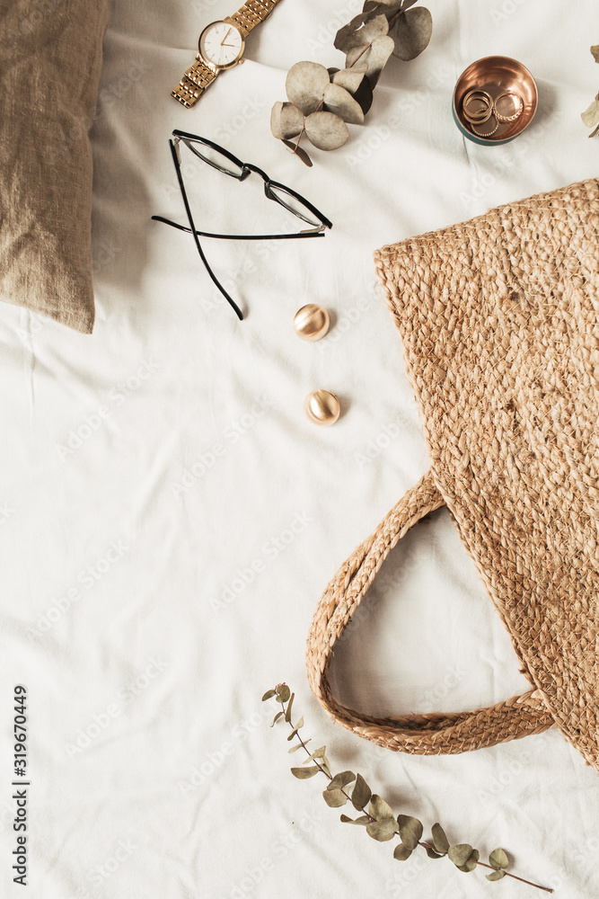 Fototapeta premium Fashion women accessories, straw bag, pillow, eucalyptus branches on white linen. Flat lay, top view fashion blogger concept for social media, website, blog.