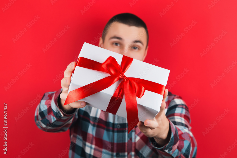 A man in a plaid shirt on a red background, holding a gift in his hands. Surprise on Valentine's Day or women's day. A man in a plaid shirt on a red background, holding a gift in his hands. Surprise on Valentine's Day or women's day.