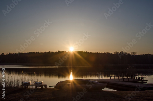 Sunrise on the lake in spring. Boats silhouettes and the rays of the rising sun.